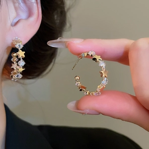 Close-up of a gold star-shaped C-hoop earring with sparkling zircon on a model's ear
