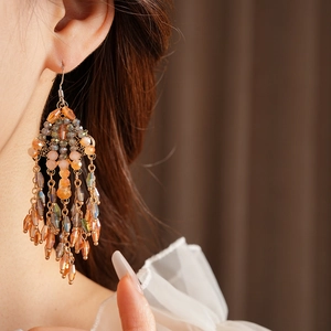 Close-up of golden tassel earrings with amber crystal beads worn by a model
