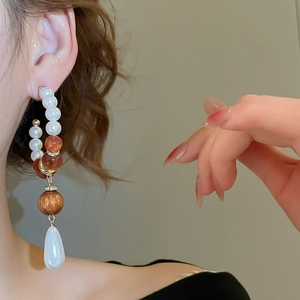 Detail of long pearl drop earrings featuring amber beads and teardrop pendant on model