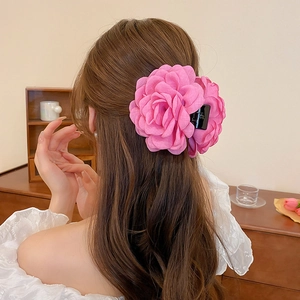 Pink fabric rose hair claw clip shown on a model with long dark wavy hair