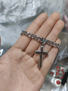 Detail of silver stainless steel cuban chain necklace with cross pendant held by hand