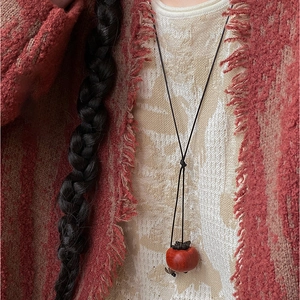 Detail of persimmon pendant necklace on vintage cardigan with minimalist black cord