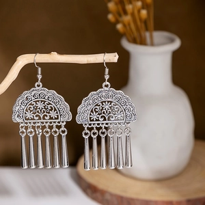 Detail of silver vintage ethnic tassel earrings hanging on a natural wooden branch