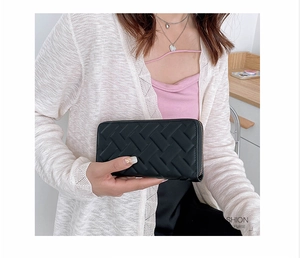Close-up of black woven leather long wallet held by a model in a stylish modern setting