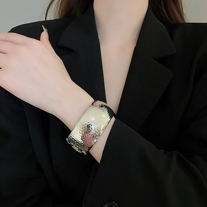 Detail of wide hammered gold metal cuff bracelet on model with black suit