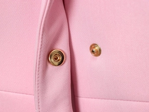 Dettagli del completo rosa con pantaloni a zampa, bottoni a pressione dorati e tessuto