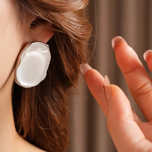 Close-up of a white oval resin earring with silver border on a model with a brown backdrop