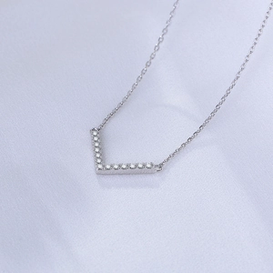 Macro detail of V-shaped silver pendant set with sparkling cubic zirconia on textured fabric