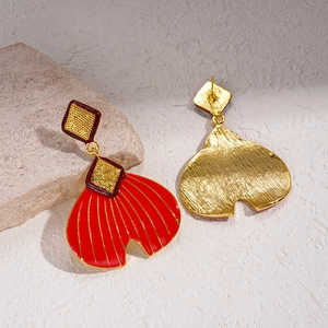 Detailed close-up of red enamel and gold fish-tail earrings on a natural stone base