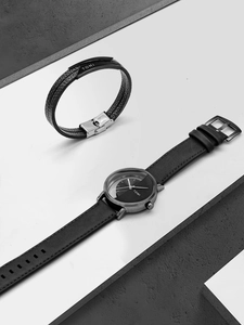 Detail of TOMI black leather watch and multi-layer bracelet with minimalist logo hardware