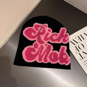 Detail of black knitted beanie with pink Rich Mob lettering on a textured background