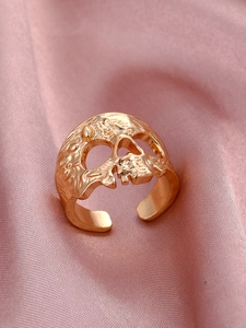 Dettaglio dell'anello con teschio dorato e incisioni su tessuto di seta rosa