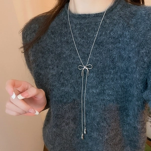 Close-up of a silver bow necklace with long tassels on a model dark sweater