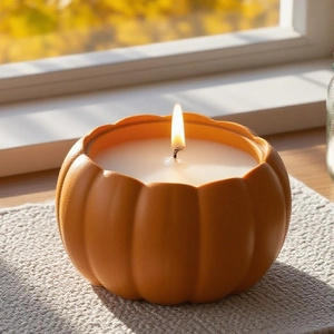 Orange pumpkin shaped scented candle in a matte finish resin container on a wooden windowsill