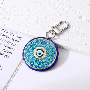 Close-up of blue geometric evil eye keychain with silver spring clasp on a white surface