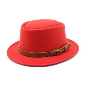 Detail view of a bright red wool felt boater hat featuring a brown leather strap and gold buckle