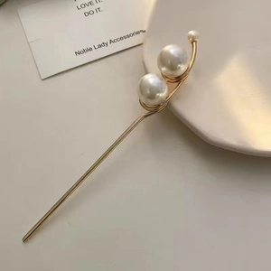 Detail of minimalist gold hairpin featuring elegant white pearls on a ceramic dish