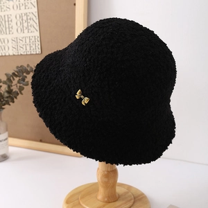 Detailed close-up of a black faux shearling bucket hat with a gold bow accent on wood