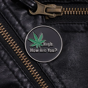 Detail of round black enamel pin with green leaf and High How Are You text on leather