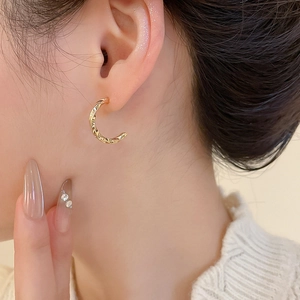 Close-up of golden twisted C-shaped hoop earring worn by a model for an elegant look