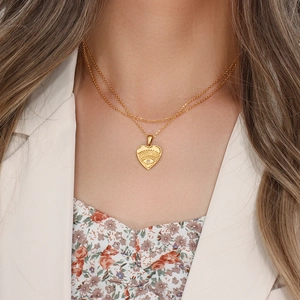 Close-up of gold double-layer necklace featuring heart pendant with eye detail and crystal