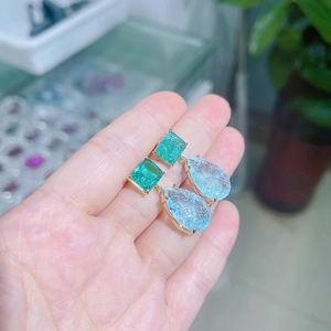 Detail of green square and light blue teardrop gemstones set in gold earring