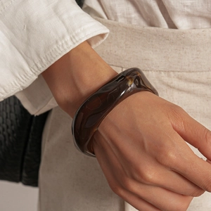 Détail d'un bracelet en acrylique marron translucide au design torsadé porté au poignet