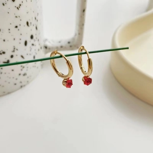 Elegant gold hoop earrings with red round gemstone pendants shown in a lifestyle setting