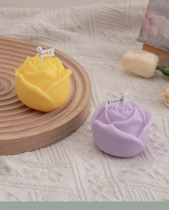Top view of yellow and purple rose-shaped scented candles on a knitted tablecloth