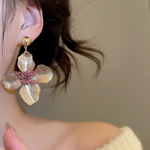 Close-up of a large gold flower earring with a pink center petal worn by a model