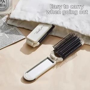Detail of compact cream-white folding hairbrush showing the built-in mirror and massage teeth