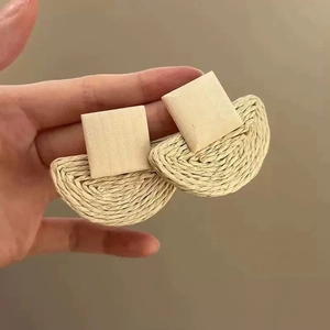 Detail of bohemian raffia woven earrings with beige square stud and textured fan-shaped drop