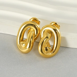Macro detail of gold-plated twisted chain earrings with heart detail on grey fabric