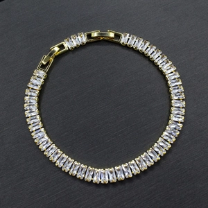 Macro shot of gold bracelet featuring rectangular white cubic zirconia stones on black background