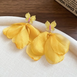 Macro shot of yellow fabric butterfly earrings with delicate tassel on a white tray