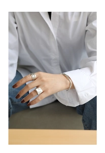Detail of silver wavy open bangle and textured wide rings on wrist with casual outfit