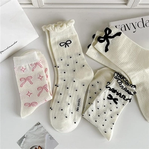 Detail of cream mid-calf socks featuring black polka dots and delicate bow accents