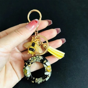 Detailed view of resin letter keychain with dried flowers, gold bee charm and yellow tassel