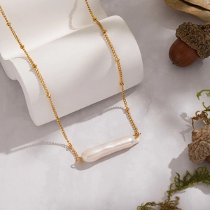 Baroque pearl pendant necklace on gold chain over marble background with acorn decor