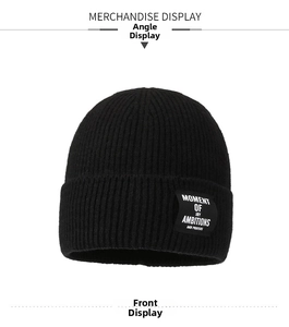 Detailed close-up of a black ribbed knit beanie with a stylish white woven slogan patch