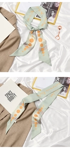 Close-up of a light green French style silk scarf with sun patterns and elegant ties