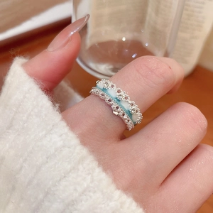 Detailed view of silver open ring with blue enamel flower and hollow filigree design