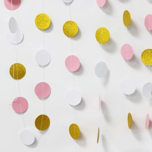 Close-up of glitter gold, pink, and white paper circle garland hanging on a white wall