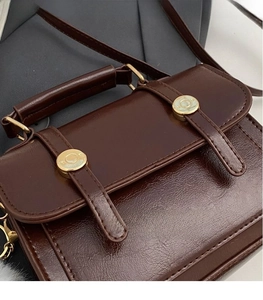 Detail of dark brown leather crossbody bag featuring dual golden circular hardware accents