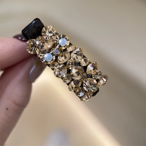 Gros plan d'une pince à cheveux noire avec des strass champagne étincelants en main