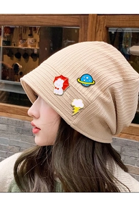 Detail of beige knitted hat featuring rabbit, planet, and cloud enamel pins