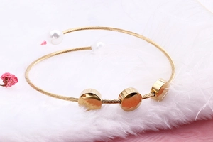 Close-up of golden spiral cuff bracelet with pearls and round discs on white feathers