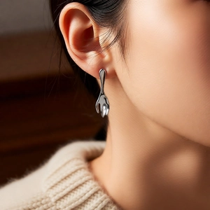 Close-up of a silver fork and spoon earring worn by a model in soft lighting