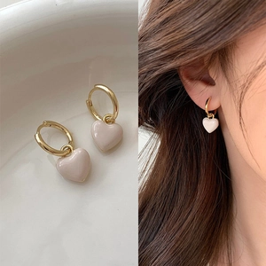 Détail de boucles d'oreilles cœur dorées avec émail rose posées sur un plateau blanc