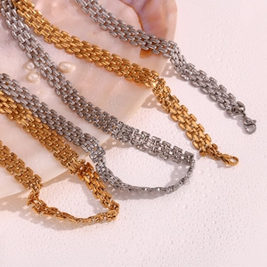 Close-up of gold and silver woven metal watchband chains on pink background